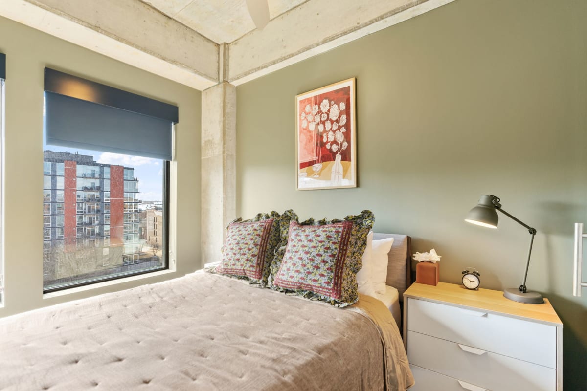 Sink into your cozy bed with soft linens and colorful pillows while city views frame your restful retreat.
