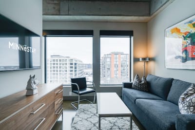 A contemporary living room featuring a gray sofa, decorative cushions, and large windows with a city view.