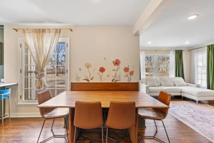 A dining area featuring a wooden table, leather chairs, and a flower accent wall with a view outside.