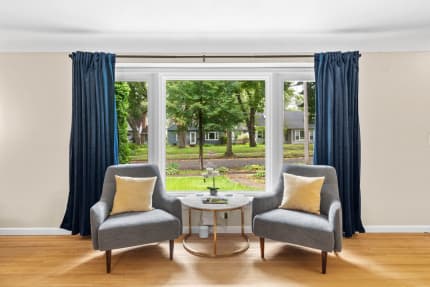 Cozy room with gray chairs, navy curtains, and a view of greenery through large windows.
