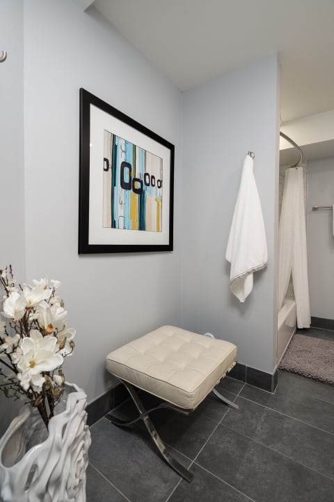 Stylish bathroom corner with a tufted ottoman, abstract artwork, and decorative flowers.