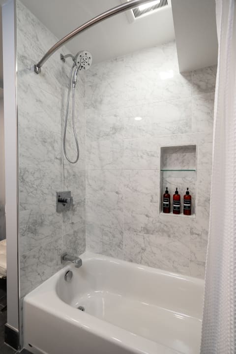 A sleek and modern shower area featuring marble walls and a white bathtub.