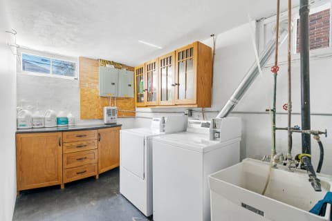 A bright basement laundry room featuring white walls, washing machines, and storage cabinets.