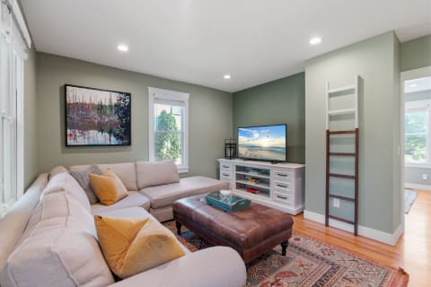 Cozy living room with a light sectional sofa, a leather ottoman, and a TV on a white media console.