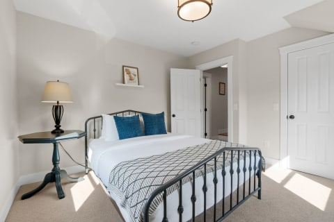 A cozy bedroom with a metal bed frame, blue accent pillows, and an octagonal side table with a lamp.