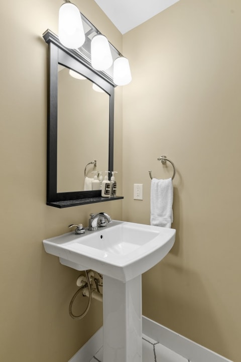 Compact bathroom featuring a white pedestal sink, black-framed mirror, and beige walls.