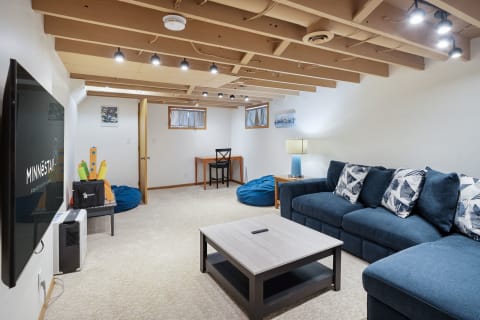 Cozy basement living room with blue sectional sofa, coffee table, and bean bags.
