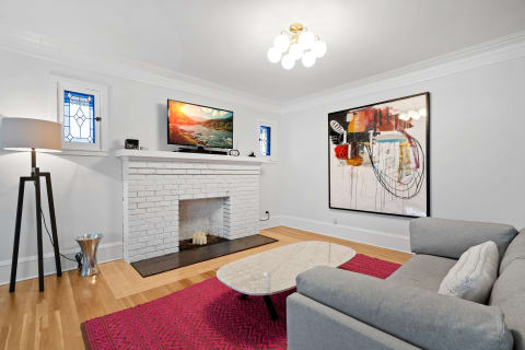 Modern living room with a white brick fireplace, television, and colorful artwork.
