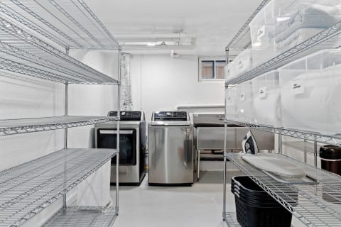 A tidy laundry room with wire shelves, washing machine, dryer, and storage bins.