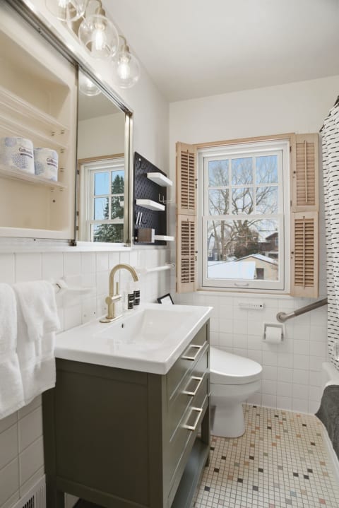 A contemporary bathroom featuring an olive green vanity, white tiles, and a view of snowy trees through a window.
