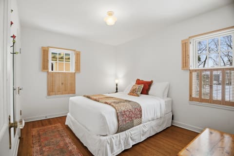 A cozy bedroom with white linens, a decorative throw, and wooden shutters, creating a peaceful atmosphere.