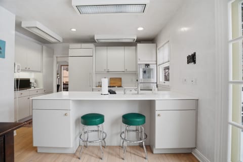 Modern white kitchen featuring an island with green stools and contemporary appliances.