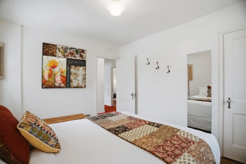 A cozy bedroom featuring a patterned quilt, floral artwork, colorful hooks, and a mirror.
