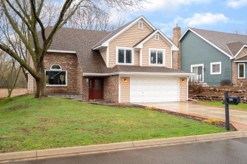 Two-story house with a brick and beige siding exterior, large windows, and a two-car garage.