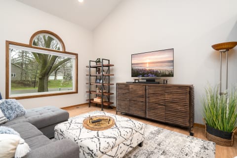 A modern living room featuring a gray sectional sofa, coffee table, TV, and decorative shelving.