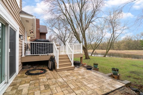 Backyard scene with a wooden deck, stone patio, and view of a river.
