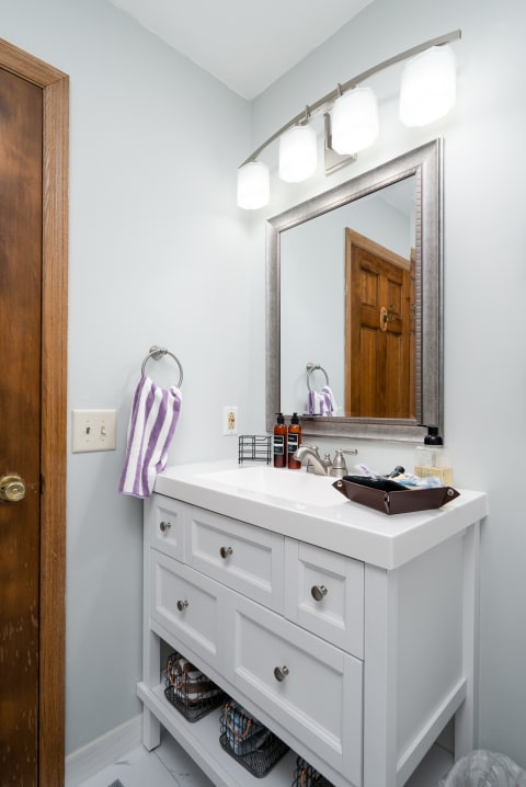 A contemporary bathroom vanity featuring a white countertop, stylish light fixture, and neat organizational elements.
