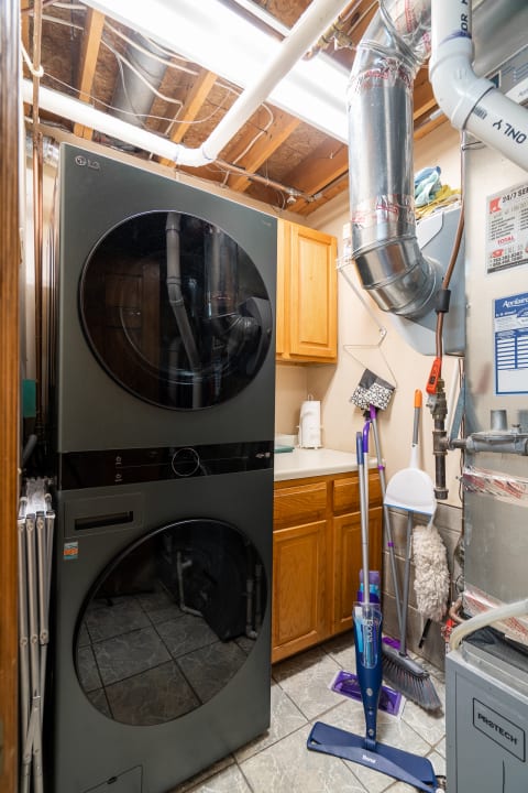 A sleek black LG washer and dryer in a tidy laundry room with wooden cabinets and cleaning supplies.