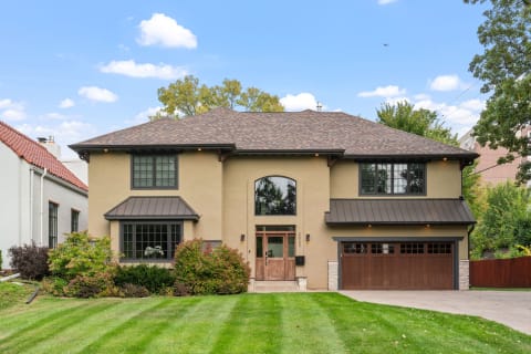 A contemporary two-story home with beige stucco, dark accents, and a lush green lawn.