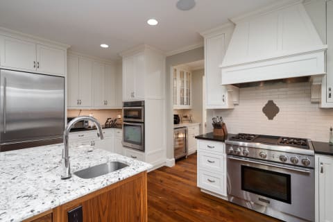 A contemporary kitchen featuring marble countertops, white cabinetry, and stainless steel appliances.