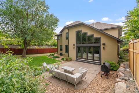Backyard of a modern home featuring a patio, greenery, and a tree.