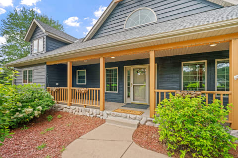 A two-story house with a blue exterior and a welcoming front porch, surrounded by greenery.