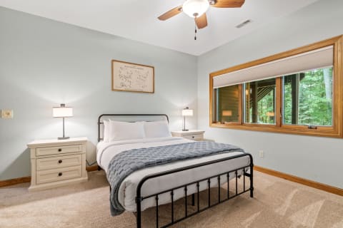 A cozy bedroom featuring a metal bed frame, nightstands, and a large window with a view of the forest.
