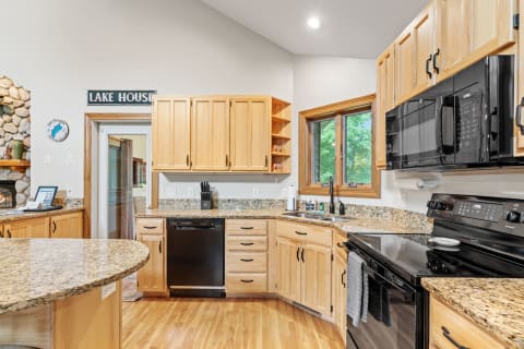 Kitchen with light wood cabinets, granite countertops, and a view of trees outside from the window.