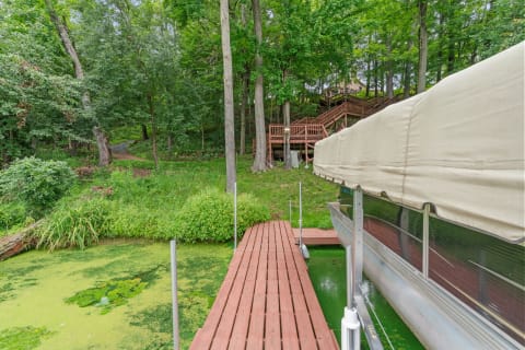 Wooden dock leading into a pond with green vegetation and a wooden deck in the background.