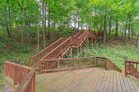 Wooden deck and ascending staircase surrounded by trees and greenery.