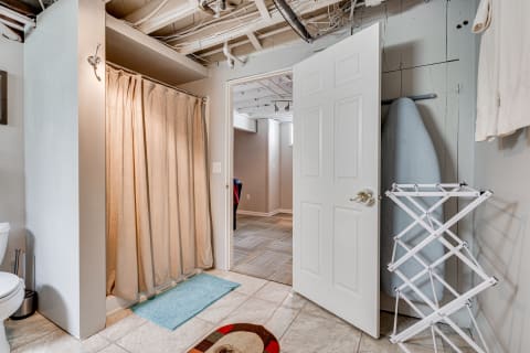 Interior view of a basement bathroom with a shower curtain and open door leading to a second room.