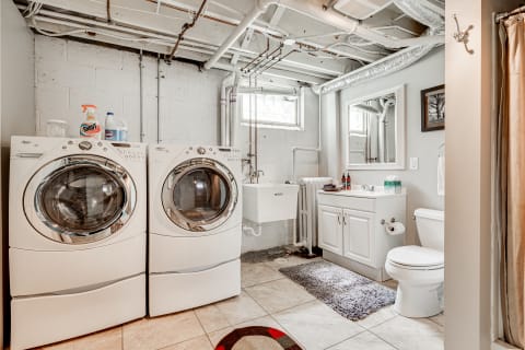 A clean and organized laundry room with washing machines, a utility sink, and a bathroom area.