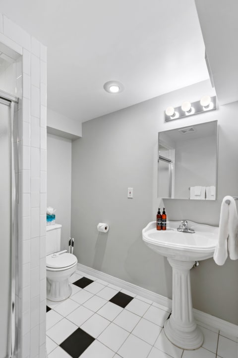 A minimalist bathroom with gray walls, black and white tiled floor, a pedestal sink, and a glass shower.