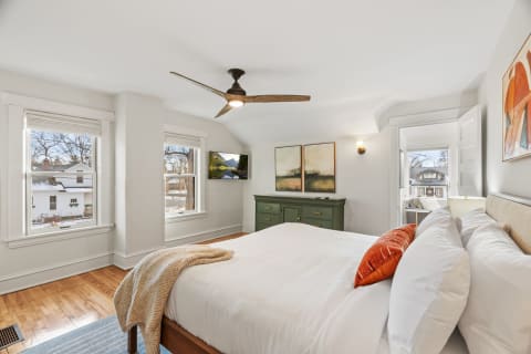 A modern bedroom featuring a white bed, wooden flooring, and colorful artwork.