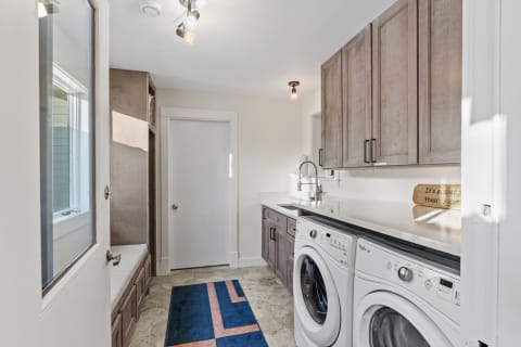 A spacious and well-organized laundry room with modern appliances, ample storage, and a cozy bench.