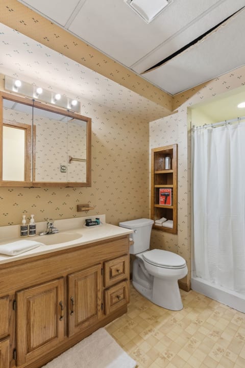 Cozy bathroom with wood vanity, shower curtains, and decorative shelving.