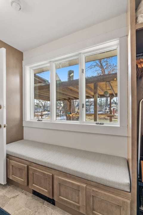 A window seat with a herringbone-patterned cushion overlooking a peaceful courtyard with a wooden pergola.
