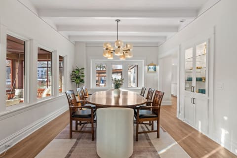 A modern dining room with a wooden table, upholstered chairs, and a striking chandelier under soft natural light.