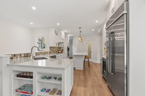 A spacious modern kitchen featuring white cabinets, a colorful backsplash, and an island with games stored underneath.