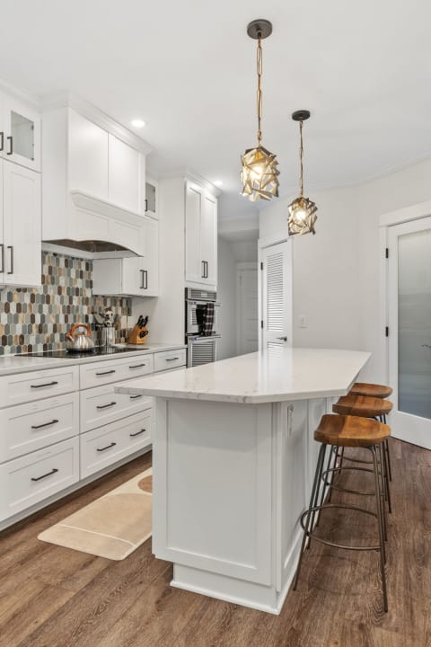 A contemporary kitchen featuring white cabinets, marble countertops, colorful tile backsplash, and stylish pendant lighting.