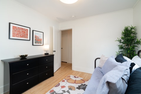 A cozy bedroom with a black dresser, two pieces of framed artwork, and a bed with decorative pillows.