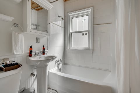 Bright and clean bathroom with white tiles, a pedestal sink, and a bathtub.