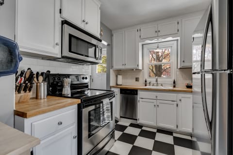 Modern kitchen with white cabinets, a black stove, and wooden countertop, featuring a checkered floor and natural light from a window.