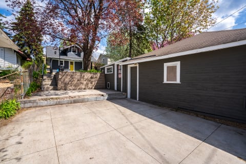 A dark wooden structure with a driveway and surrounding greenery, featuring a patio area in front.
