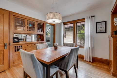 Cozy dining room featuring a wooden table, gray chairs, and a wooden hutch with decorative items.