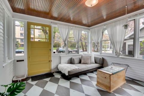 A sunroom featuring a yellow door, gray couch, and wooden accents.