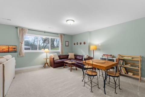 A cozy living room featuring a light couch, burgundy sofa, wooden dining table, and large windows.