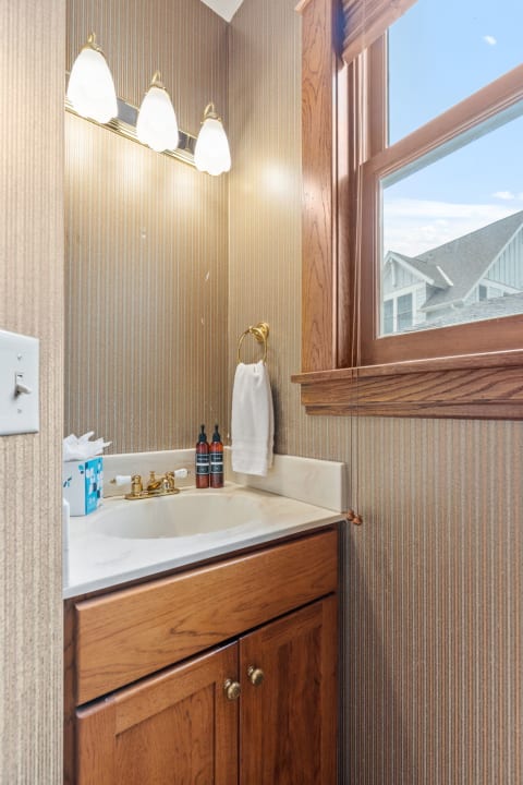 A beautifully designed half-bathroom with a marble countertop and wooden cabinets, illuminated by stylish light fixtures.
