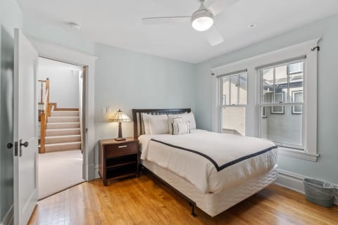 Cozy bedroom featuring a bed with white bedding and a dark wooden headboard, along with a nightstand and a window.