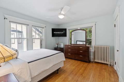 Modern bedroom with blue walls, wooden floor, dresser, mirror, and flat-screen TV.